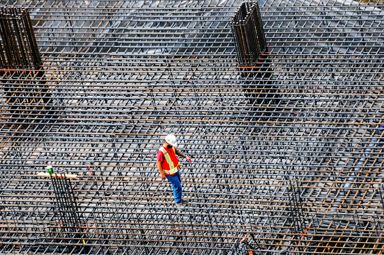 Construction worker in a hard hat and safety vest walking a rebar grid on a commercial jobsite, the kind of project where The Guy That Gets You Paid helps contractors and suppliers collect unpaid invoices