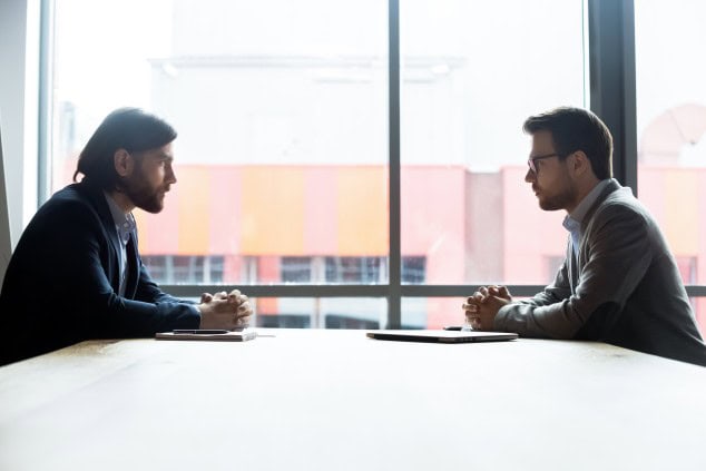 Two businessmen negotiating across a conference table in a bright office