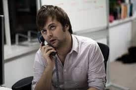 Frustrated businessman waiting on hold on the phone at his desk