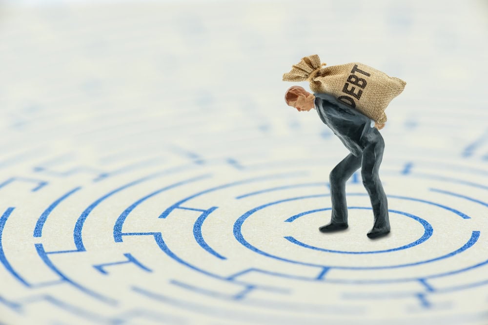 Businessman carrying a heavy bag of debt through a maze, representing unpaid commercial debt