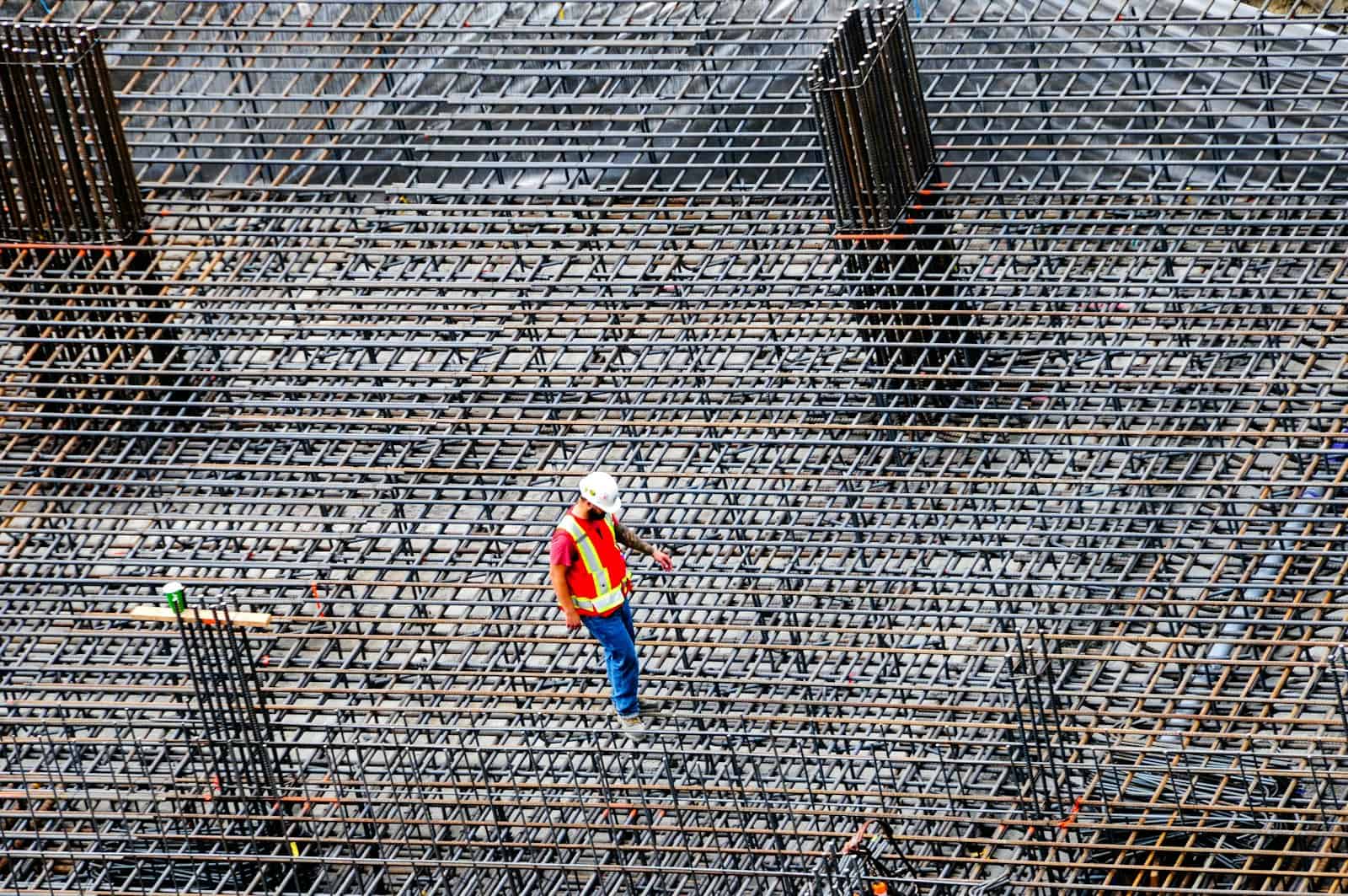 Construction worker in a hard hat and safety vest walking a rebar grid on a commercial jobsite, the kind of project where The Guy That Gets You Paid helps contractors and suppliers collect unpaid invoices
